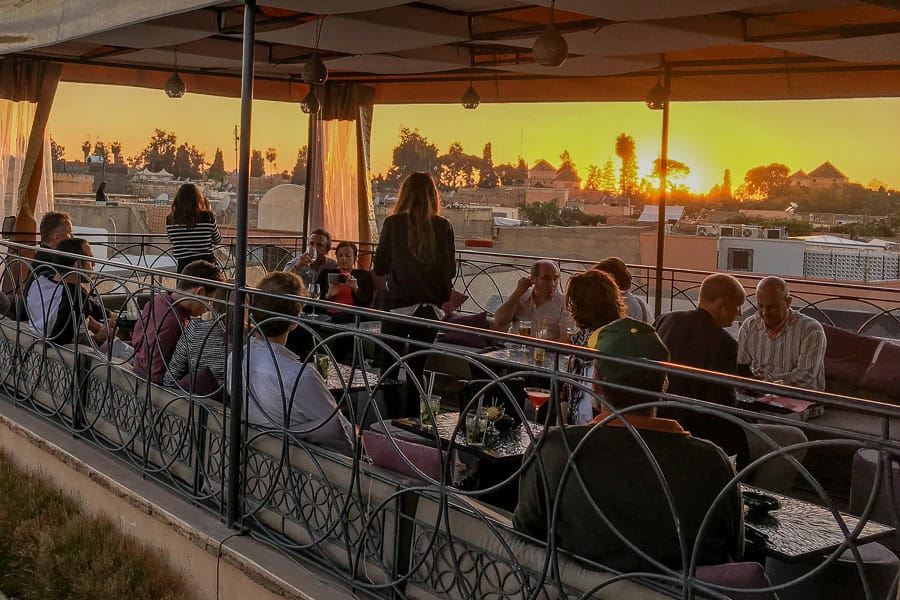 Customers in a rooftop bar enjoy a golden sunset while visiting Marrakech.