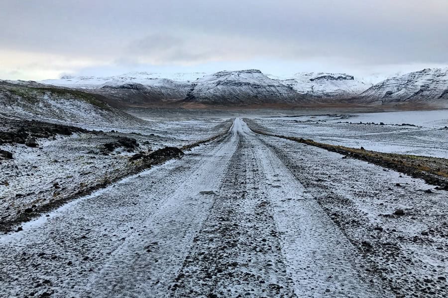 A minor snow dusted road heads towards snowcapped mountains – a common site while driving in Iceland in winter.