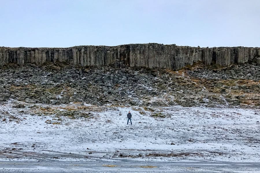 A person stands in front of Gerðuberg Cliff in icy conditions while visiting Iceland in winter.