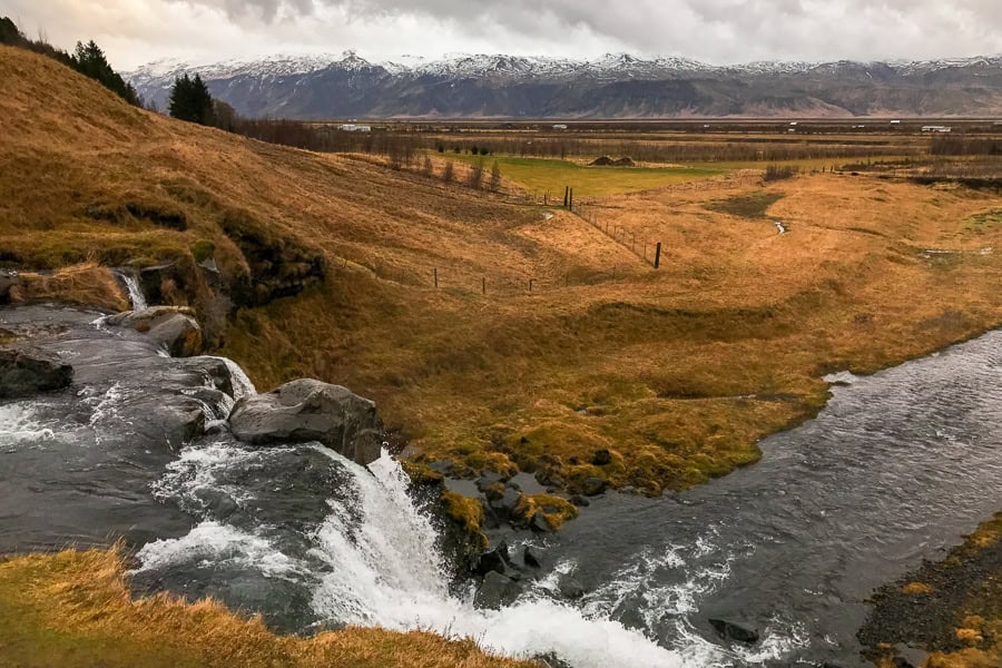 A waterfall rushes in the foreground with a mountain range in the background at Gluggafoss in southern Iceland.