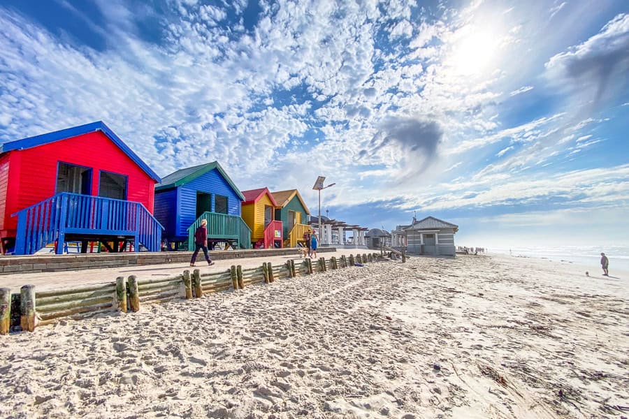 Colourful Victorian beach huts line the sand on a morning at Muizenberg Beach in South Africa. 