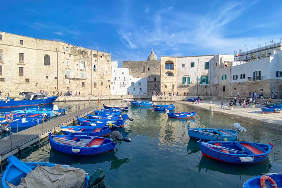 Blue boats bob on a small harbour surrounded by old stone buildings in Monopoli’s Old Port.