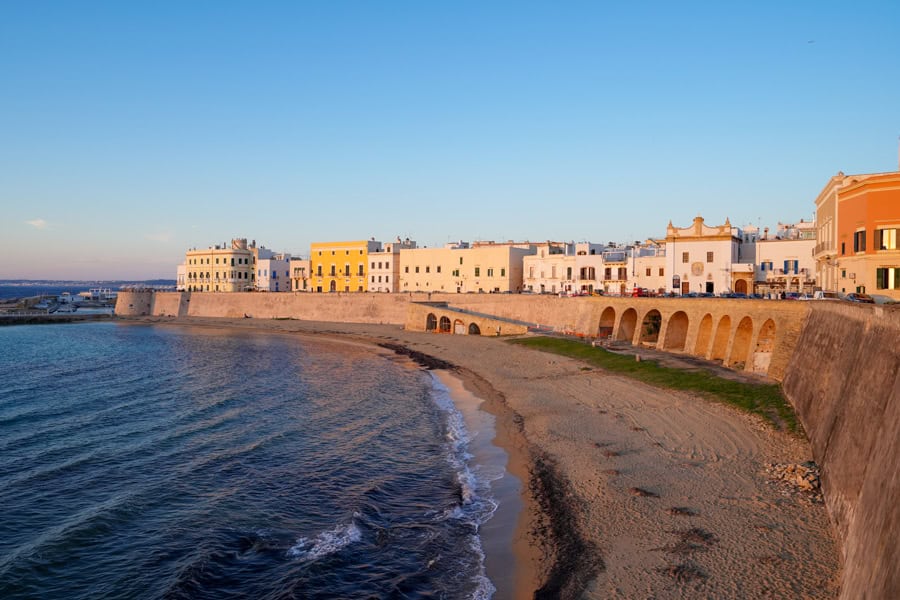 Buildings curve around a wall above a beach in Gallipoli, one of the best places to visit in Puglia.