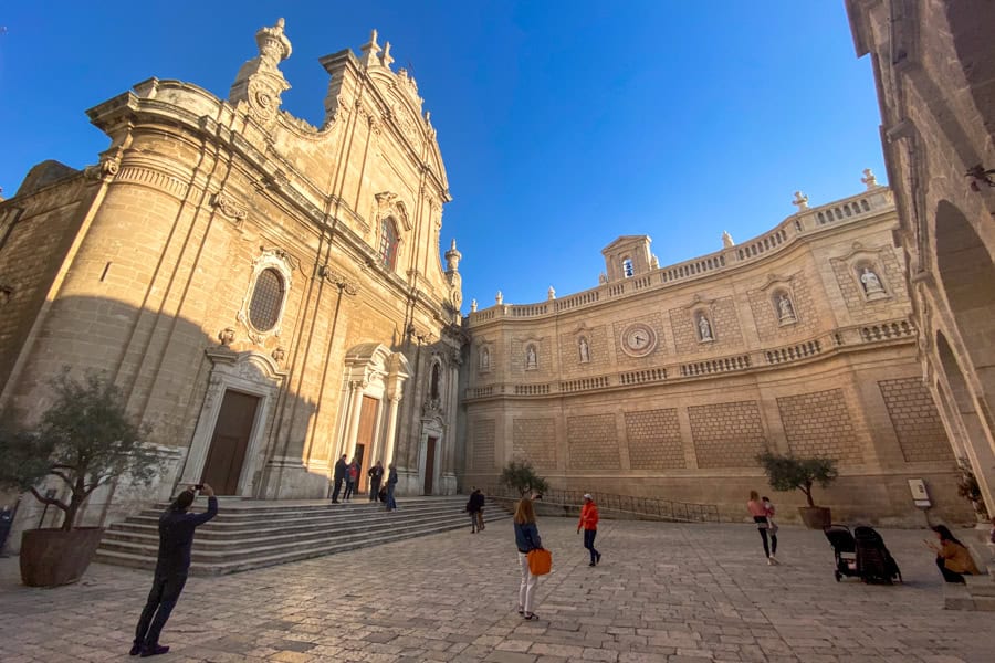 People stand outside the creamy stone walls of the cathedral, one of Monopoli’s main sites on a Puglia visit.