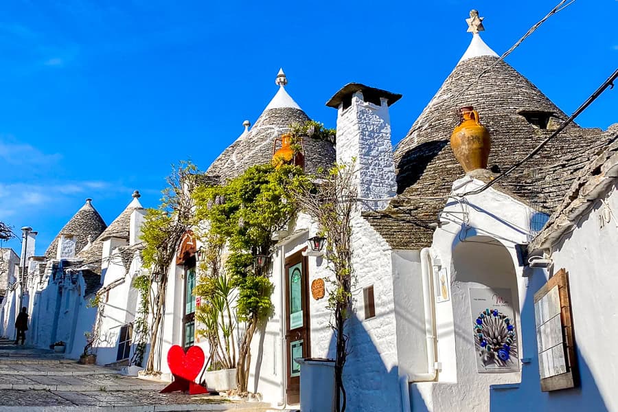 White houses with pointed roofs rise up a street in Alberobello on our Puglia road trip.