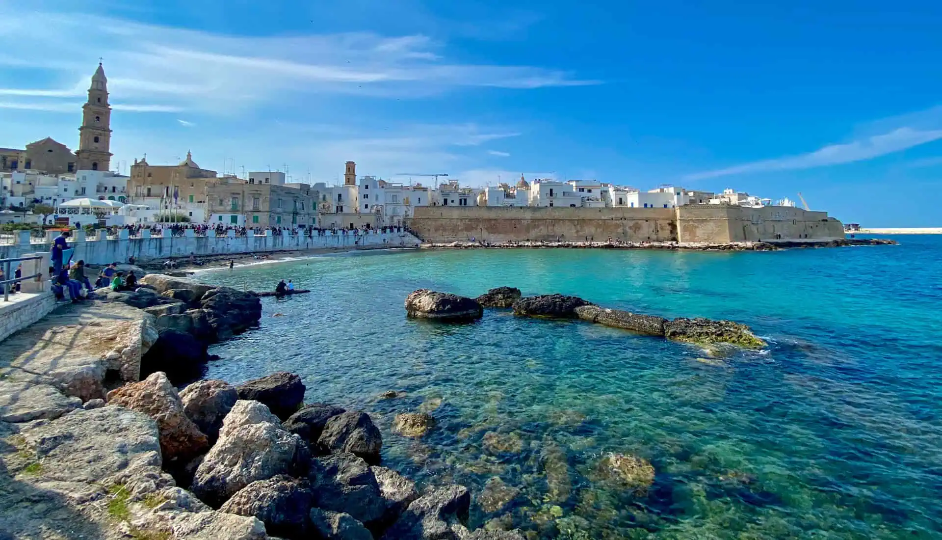 A body of water with rocks and buildings in the background in Monopoli, key stop on an itinerary for Puglia.