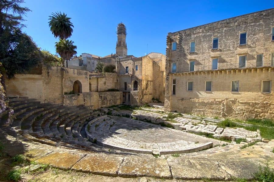 An old stone building backs a semi-circular, stone-cut Ancient Roman theatre in Lecce.