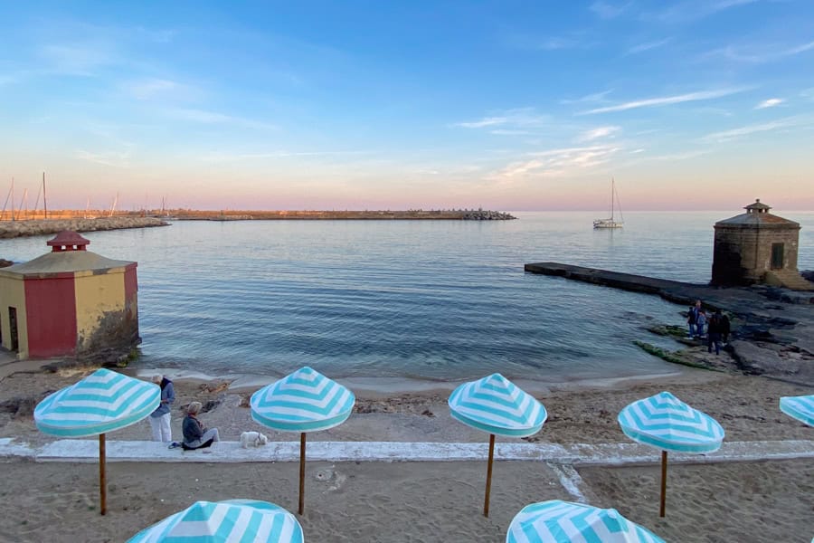 Blue striped umbrellas line a small beach at twilight in Leuca.