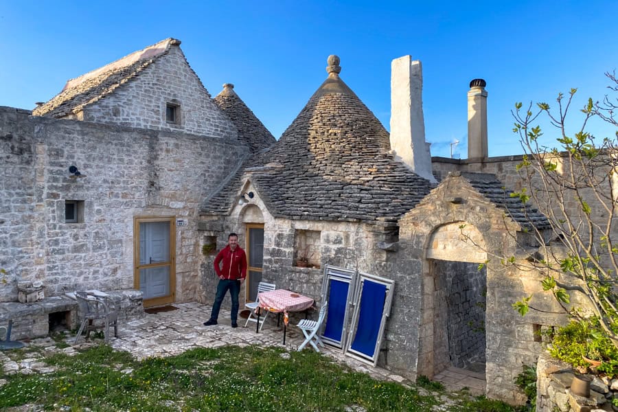 A man stands outside a stone cottage with a pointed roof in Val Ditria.