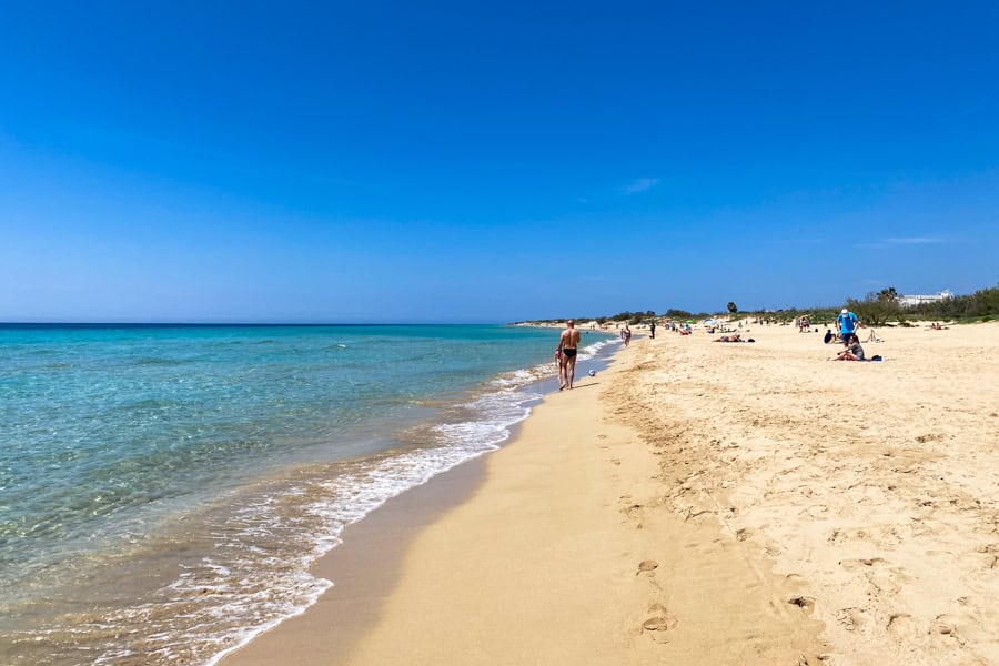 A beach of bright yellow sand with people walking on it.