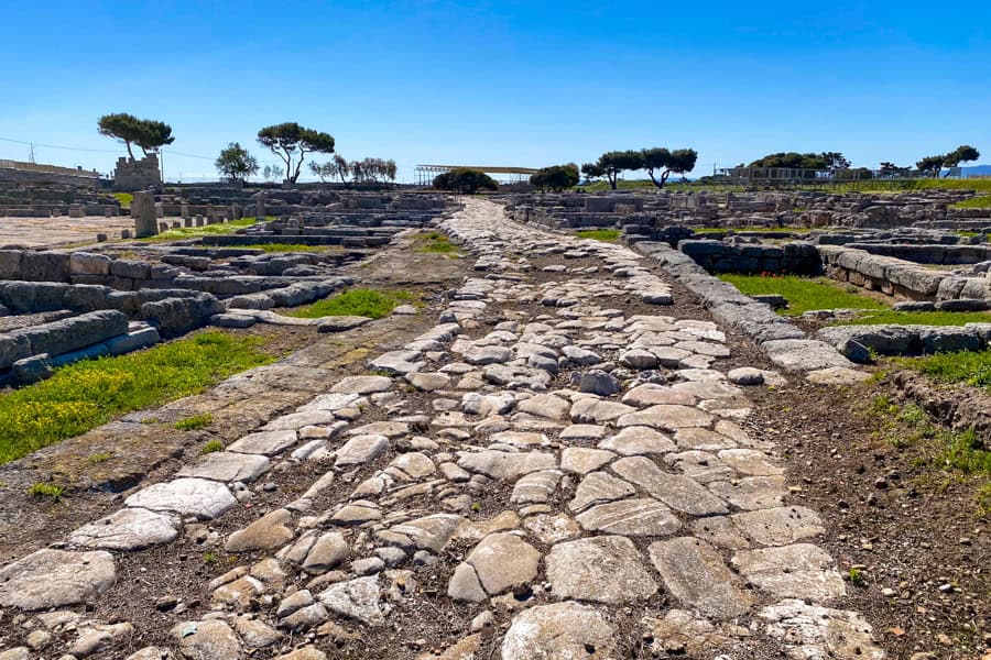 An ancient cobbled stone road winds towards trees at Egnazia, one of the oldest places to visit in Puglia.