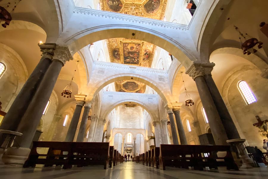 Tall columns support white marble beams under a gold leaf ceiling in Bari Cathedral.