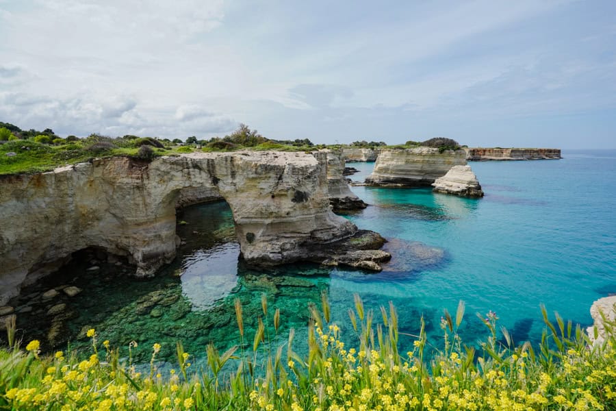 Rock formations rise from blue waters on a Puglia road trip.